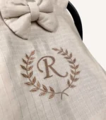 Bej tek kat müslin kumaştan fırfırlı, kapaklı puset örtüsü; tül pencereli ve kişiselleştirilebilir nakış detaylı model.