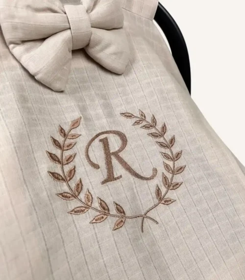 Bej tek kat müslin kumaştan fırfırlı, kapaklı puset örtüsü; tül pencereli ve kişiselleştirilebilir nakış detaylı model.