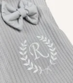 Gri örgü pike kumaştan, fırfırlı kenarlara sahip, fiyonklu kapaklı puset örtüsü.