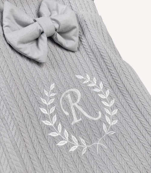 Gri örgü pike kumaştan, fırfırlı kenarlara sahip, fiyonklu kapaklı puset örtüsü.