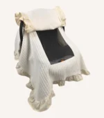 Krem örgü pike kumaştan fırfırlı, kapaklı puset örtüsü; tül pencereli ve kişiselleştirilebilir nakış detaylı model.