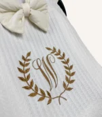 Krem örgü pike kumaştan, fırfırlı kenarlara sahip, fiyonklu kapaklı puset örtüsü.