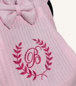 Pembe örgü pike kumaştan, fırfırlı kenarlara sahip, fiyonklu kapaklı puset örtüsü.